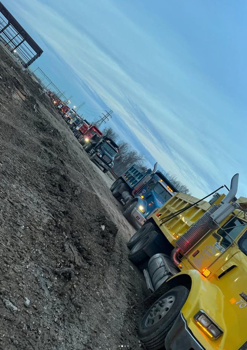 Line of dump trucks staged at a Houston-area pit at dusk for a multi-truck haul