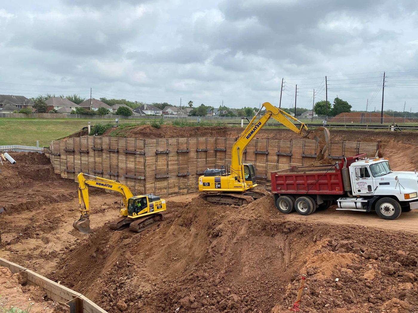 Excavators and a dump truck at a shored commercial excavation in the Houston area