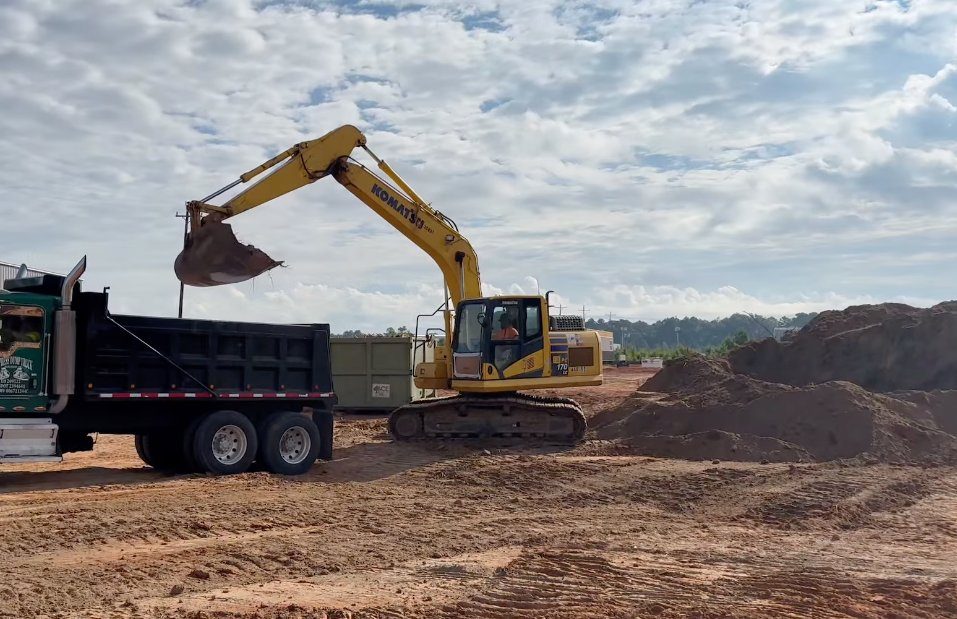 Komatsu excavator loading a Supreme Logistics dump truck with material at a Houston jobsite