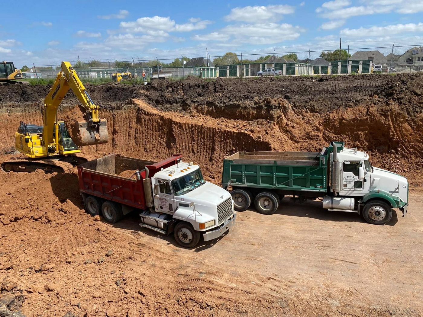 Excavator loading select fill into Supreme Logistics dump trucks in a Greater Houston dirt cut